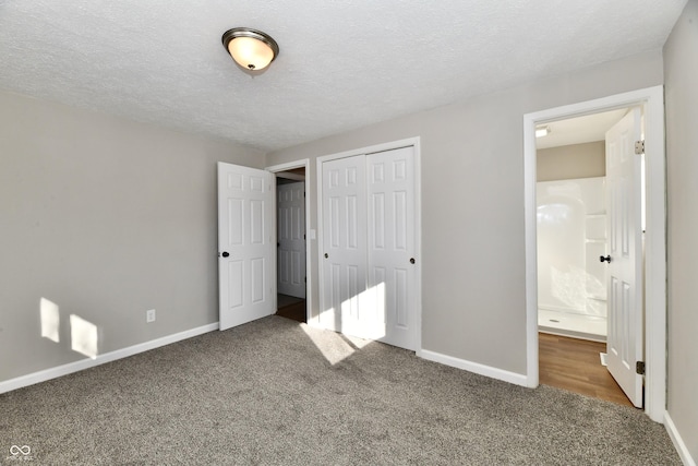 unfurnished bedroom with dark carpet, a closet, ensuite bath, and a textured ceiling