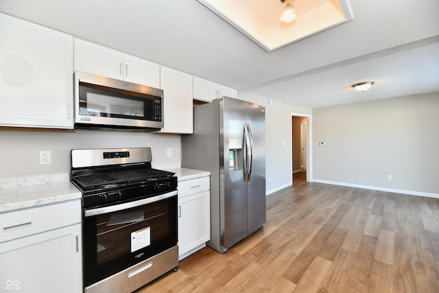 kitchen featuring light wood-type flooring, light stone countertops, appliances with stainless steel finishes, a textured ceiling, and white cabinets