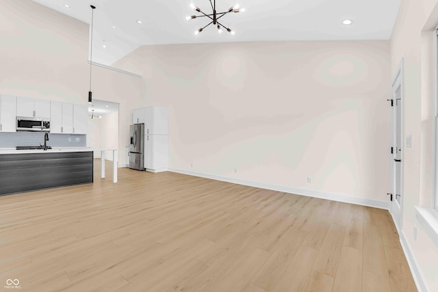 unfurnished living room with high vaulted ceiling, a notable chandelier, light hardwood / wood-style flooring, and sink