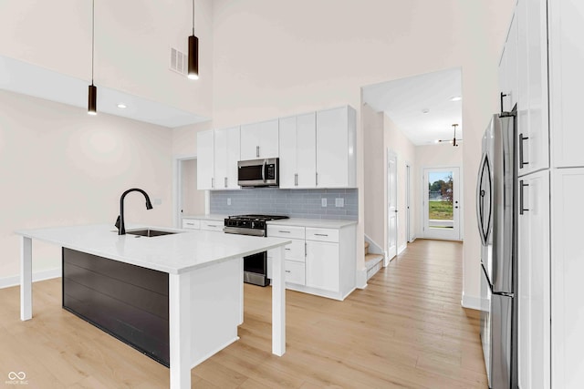 kitchen featuring pendant lighting, sink, a kitchen island with sink, stainless steel appliances, and white cabinets