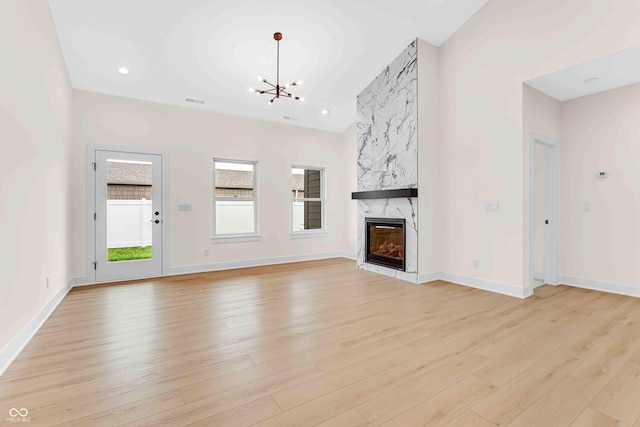 unfurnished living room featuring a large fireplace, an inviting chandelier, and light hardwood / wood-style flooring