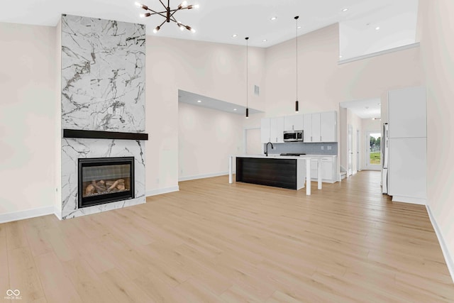 unfurnished living room with light hardwood / wood-style floors, sink, a towering ceiling, and a fireplace