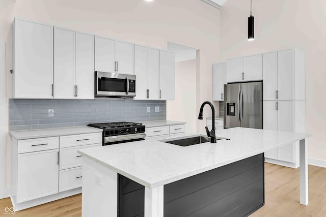 kitchen featuring a high ceiling, appliances with stainless steel finishes, sink, hanging light fixtures, and a center island with sink