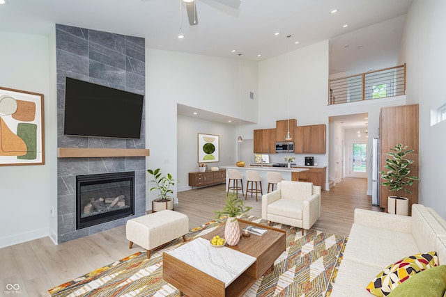 living room with light wood-type flooring, a towering ceiling, and a tile fireplace