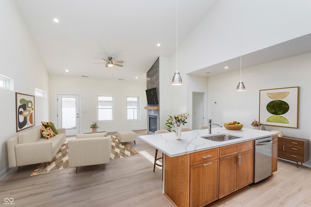 kitchen with light hardwood / wood-style floors, a center island with sink, decorative light fixtures, stainless steel dishwasher, and sink