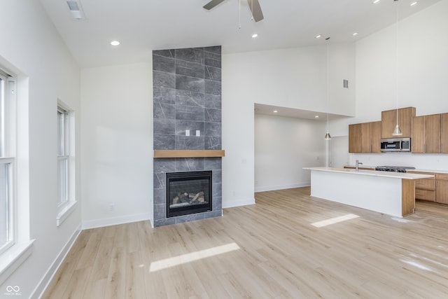 kitchen featuring a center island with sink, ceiling fan, hanging light fixtures, high vaulted ceiling, and a tile fireplace