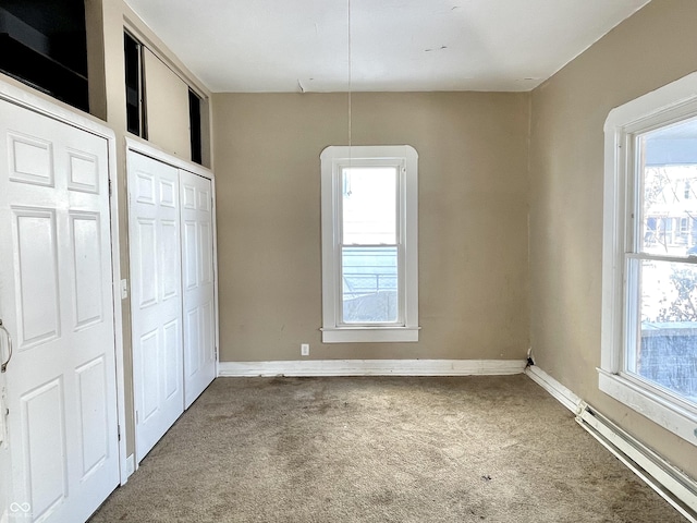 unfurnished bedroom with multiple windows, a baseboard radiator, carpet, and two closets