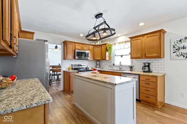 kitchen with light hardwood / wood-style floors, appliances with stainless steel finishes, a kitchen island, pendant lighting, and light stone counters