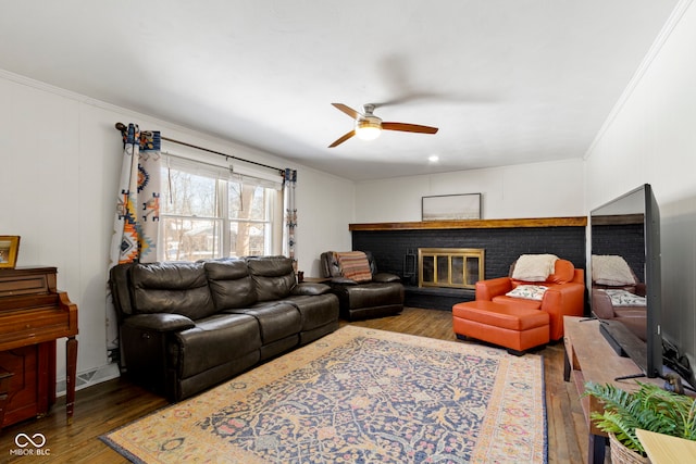 living room with a brick fireplace, hardwood / wood-style floors, crown molding, and ceiling fan