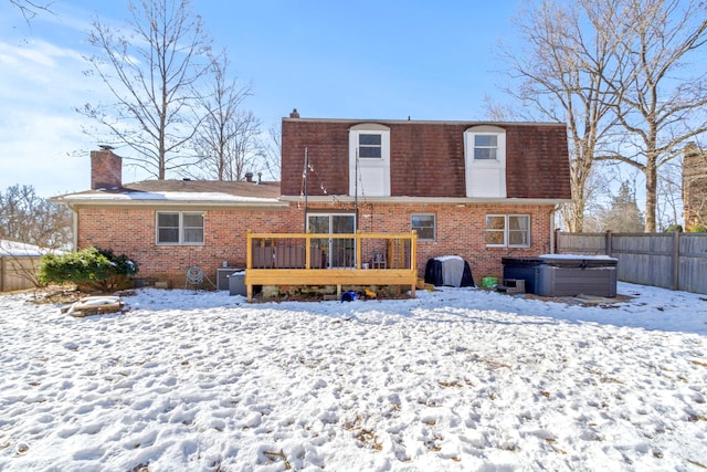 snow covered back of property with a hot tub and a deck