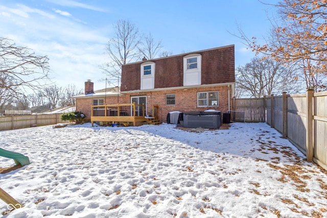 snow covered house with a wooden deck and a hot tub