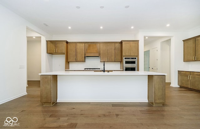 kitchen with a spacious island, wood-type flooring, range hood, ornamental molding, and double oven