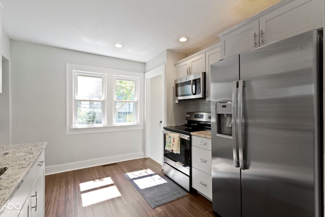 kitchen with light stone countertops, appliances with stainless steel finishes, decorative backsplash, white cabinets, and dark hardwood / wood-style floors