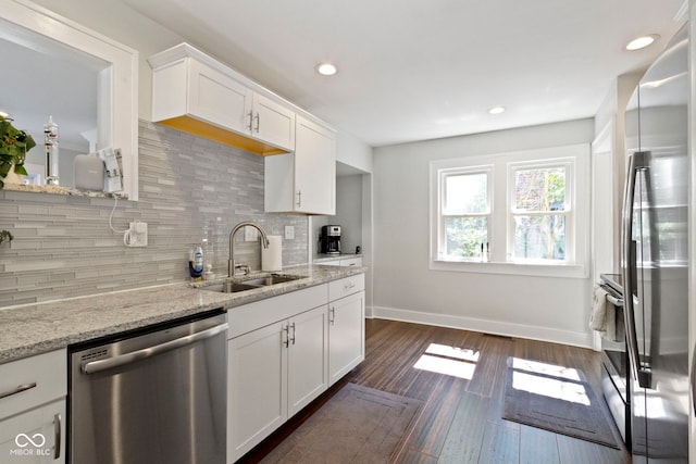 kitchen featuring appliances with stainless steel finishes, white cabinetry, decorative backsplash, sink, and light stone counters