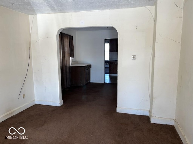 hallway with a textured ceiling and dark colored carpet