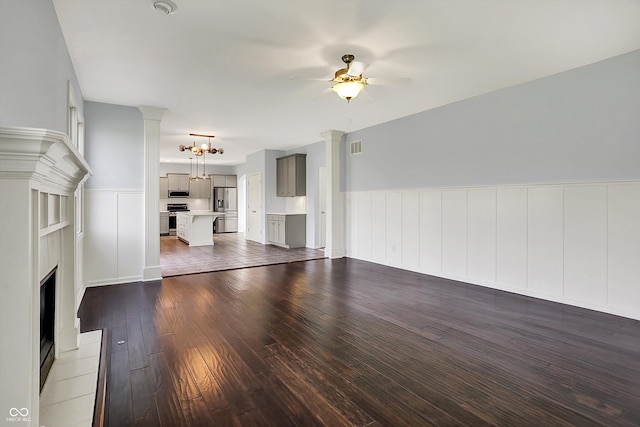 386 White Oak Ln, Greenwood, IN 46142 - unfurnished living room featuring wainscoting, decorative columns, a fireplace with raised hearth, and ceiling fan with notable chandelier