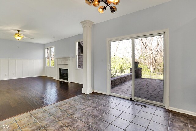 386 White Oak Ln, Greenwood, IN 46142 - unfurnished living room featuring a glass covered fireplace, visible vents, ceiling fan with notable chandelier, tile patterned flooring, and ornate columns
