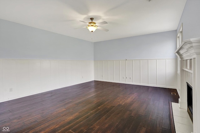 386 White Oak Ln, Greenwood, IN 46142 - unfurnished living room with a fireplace with raised hearth, wainscoting, ceiling fan, a decorative wall, and dark wood-type flooring