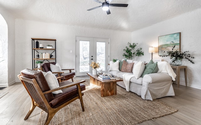 living room featuring ceiling fan, french doors, light hardwood / wood-style flooring, and a textured ceiling