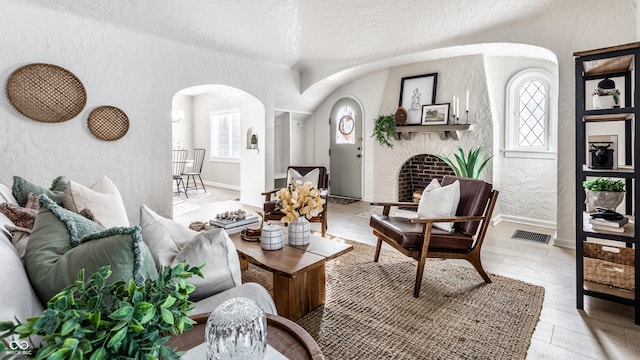 living room with light hardwood / wood-style floors, a textured ceiling, and a brick fireplace