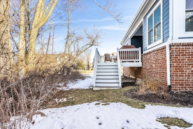 view of snowy exterior with a wooden deck, stairway, and brick siding