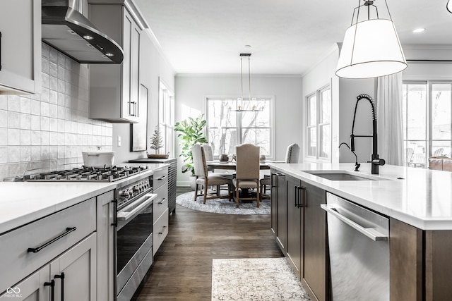 kitchen featuring hanging light fixtures, wall chimney exhaust hood, stainless steel appliances, and light countertops