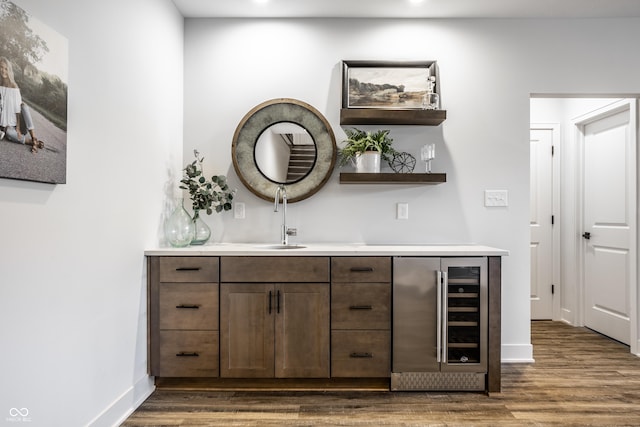 bar featuring a sink, beverage cooler, baseboards, and dark wood-type flooring