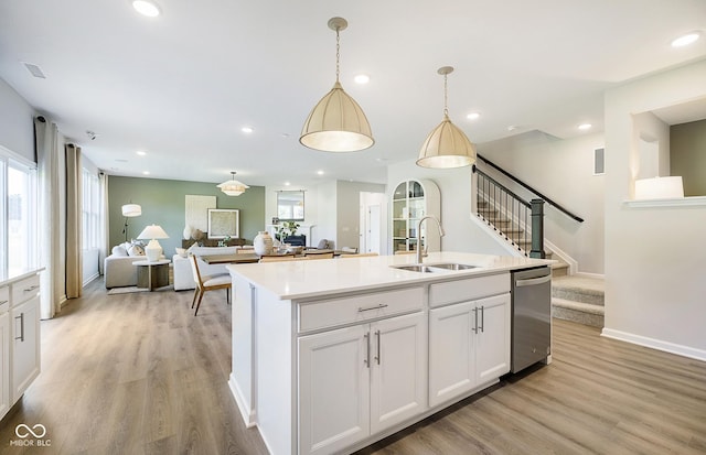 kitchen with white cabinetry, light hardwood / wood-style floors, sink, hanging light fixtures, and a center island with sink