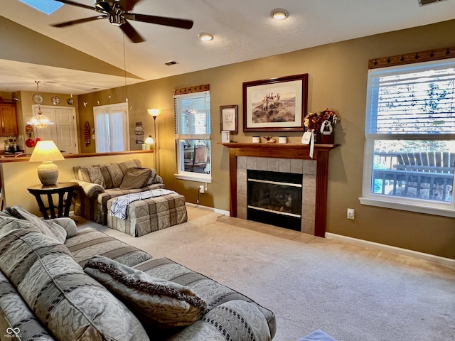 carpeted living room with ceiling fan, a tile fireplace, and vaulted ceiling