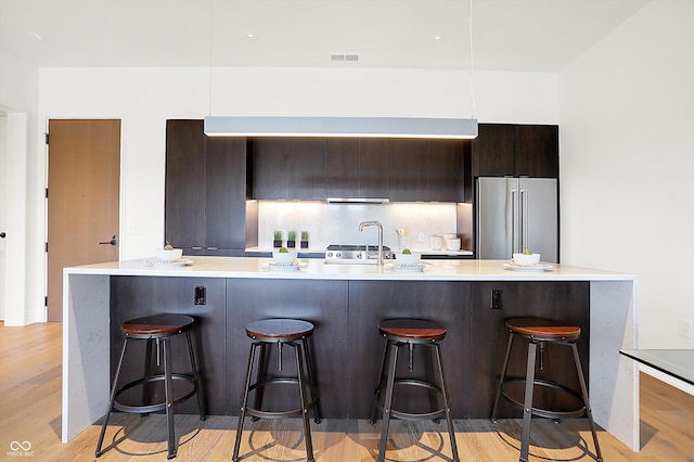 kitchen with high end fridge, a breakfast bar area, dark brown cabinetry, and light wood-type flooring