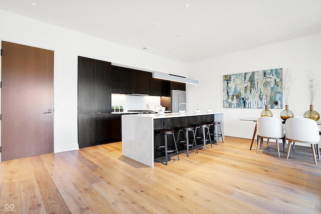 kitchen with light hardwood / wood-style floors, a kitchen bar, high end fridge, and an island with sink