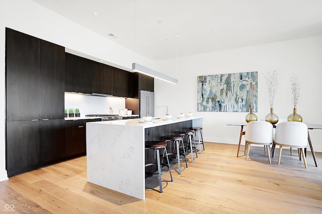 kitchen featuring light hardwood / wood-style flooring, dark brown cabinets, a center island with sink, high quality fridge, and a kitchen bar