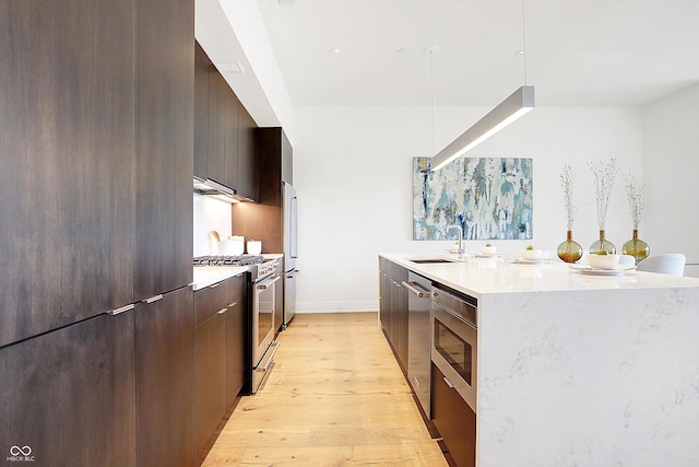 kitchen featuring sink, stainless steel appliances, light hardwood / wood-style floors, and a center island with sink