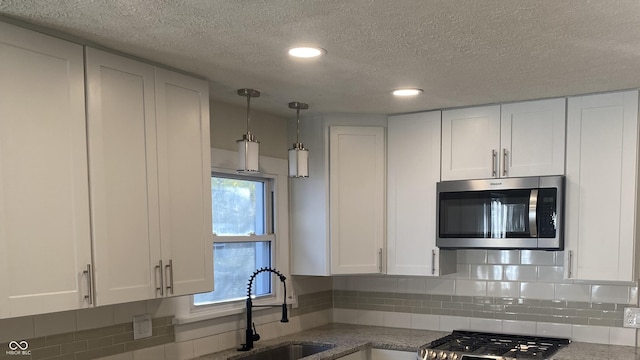 kitchen with white cabinetry, sink, decorative backsplash, hanging light fixtures, and a textured ceiling