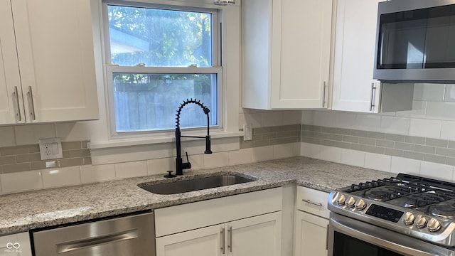 kitchen with sink, appliances with stainless steel finishes, light stone counters, tasteful backsplash, and white cabinets