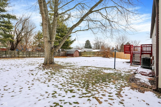 snowy yard with central AC, a storage unit, and a wooden deck