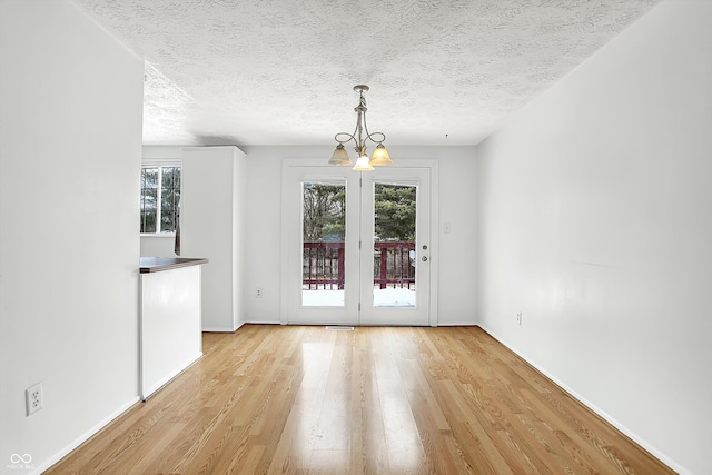 unfurnished dining area with an inviting chandelier, light hardwood / wood-style flooring, and a textured ceiling