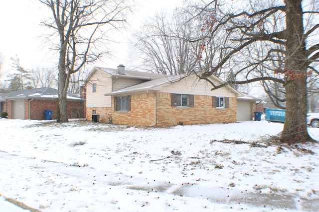 view of snow covered exterior featuring central air condition unit and a garage