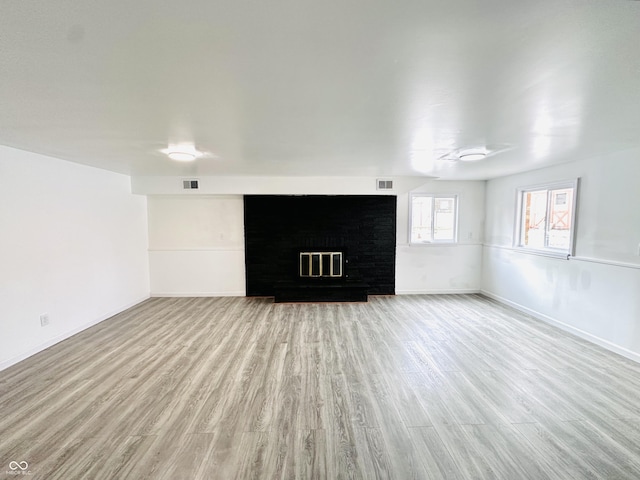 unfurnished living room with a brick fireplace and light hardwood / wood-style floors