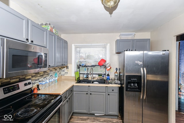 kitchen featuring wood-type flooring, gray cabinetry, sink, backsplash, and stainless steel appliances