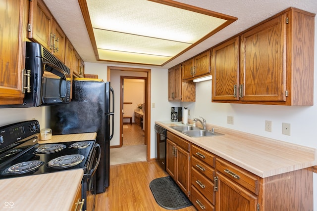 kitchen featuring sink, light hardwood / wood-style flooring, a textured ceiling, and black appliances