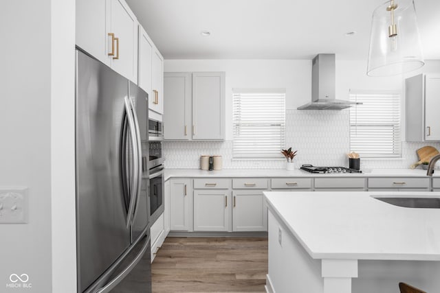 kitchen with wall chimney exhaust hood, sink, decorative light fixtures, white cabinetry, and stainless steel refrigerator