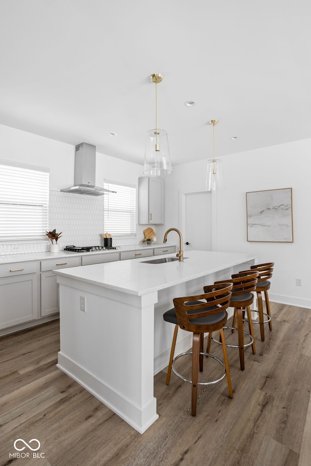 kitchen featuring wall chimney exhaust hood, a center island with sink, pendant lighting, and a kitchen bar