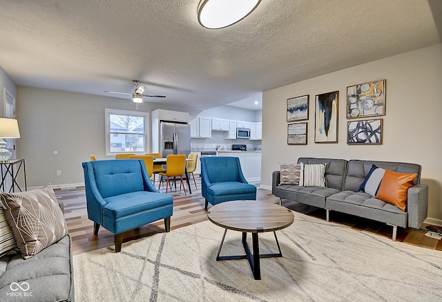 living room with ceiling fan, a textured ceiling, and light hardwood / wood-style flooring