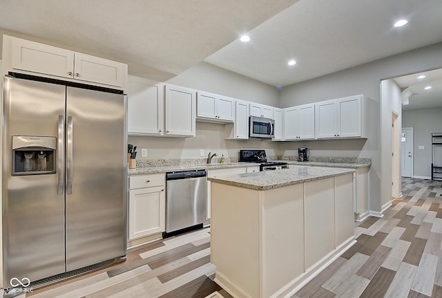 kitchen featuring a kitchen island, appliances with stainless steel finishes, white cabinetry, light stone countertops, and light wood-type flooring