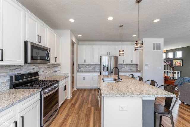 kitchen with sink, a breakfast bar area, appliances with stainless steel finishes, an island with sink, and decorative light fixtures