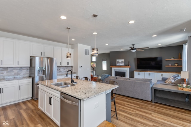 kitchen featuring sink, appliances with stainless steel finishes, pendant lighting, a kitchen island with sink, and white cabinets