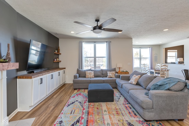 living room with ceiling fan, light hardwood / wood-style floors, and a textured ceiling