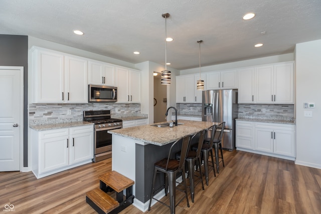 kitchen with pendant lighting, sink, stainless steel appliances, an island with sink, and white cabinets