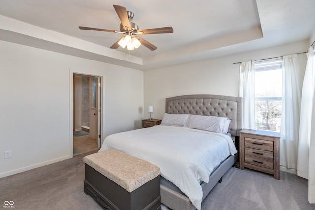 carpeted bedroom featuring ceiling fan, ensuite bath, and a tray ceiling